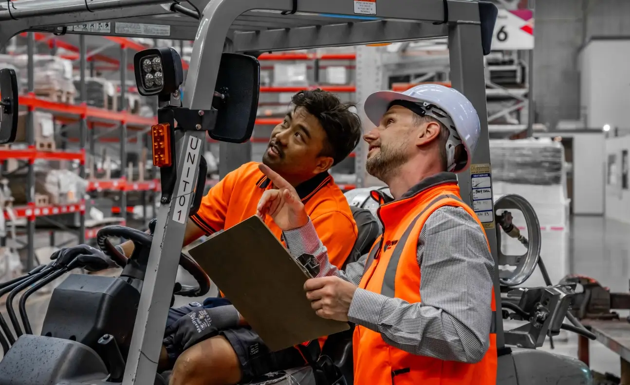 Worker inspecting forklift equipment with clipboard in warehouse storage environment